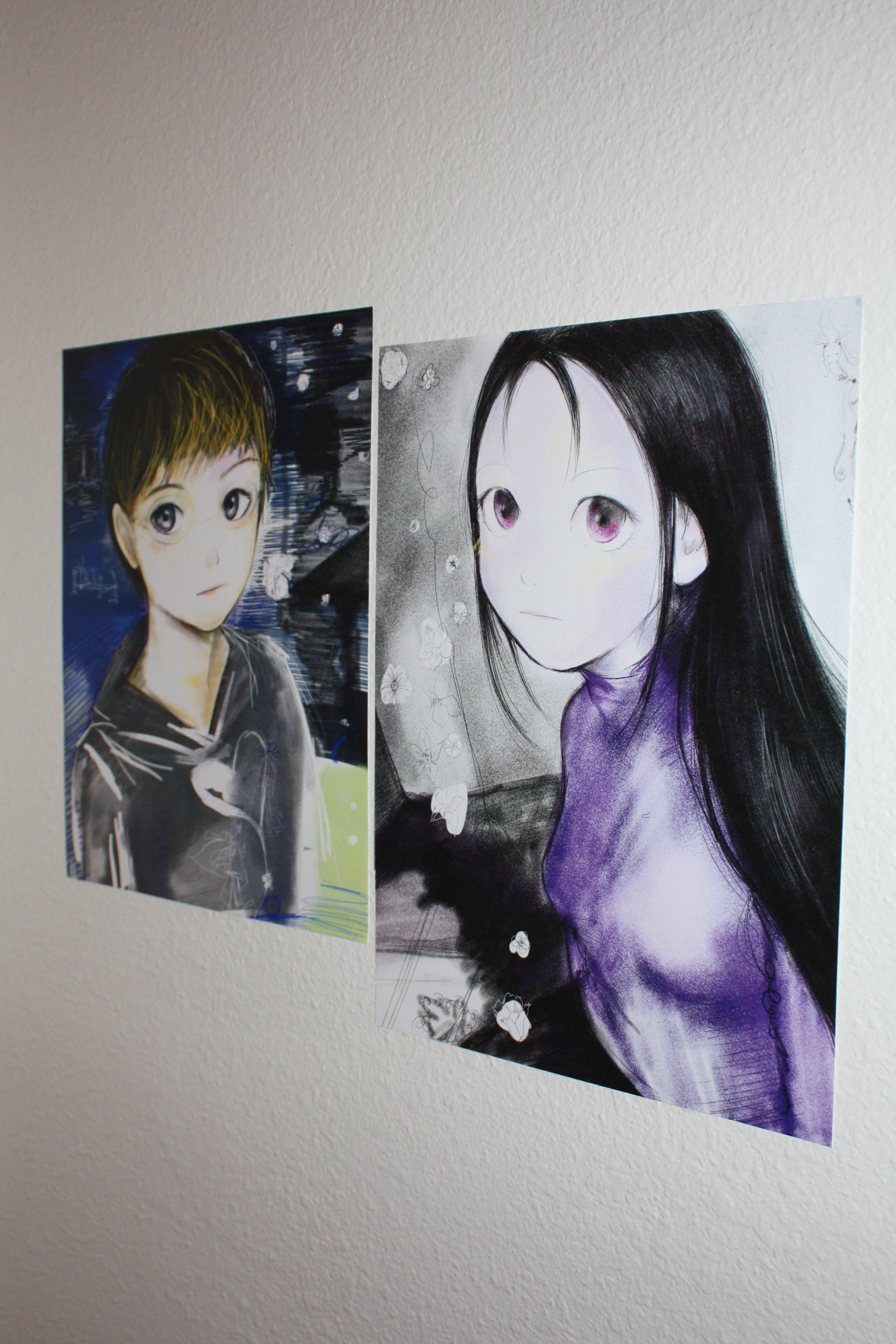 Two prints of anime figures looking at the camera hung on a wall